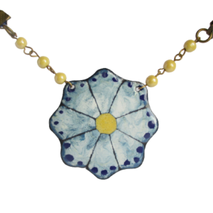 Smaltovaný náhrdelník modrý květ. Náhrdelník ve tvaru květiny na ručně opracovaném modrém plíšku v odstínech modré barvy, zavěšený na dvou stranách na řetízek se skleněnými korálky béžovožluté barvy, pokračující modrou organzovou stuhou. Komponenty jsou v mosazné barvě.