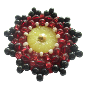Červenožlutá korálková brož. Brož vyrobená ze žlutého jabloneckého knoflíku, který je opletený pomocí měděného drátku a korálků v černé, červené a perleťové barvě. Je podšitá červenou plstí. Ze spodní strany je pomocí průhledného plastu připevněný špendlík v černé barvě.
