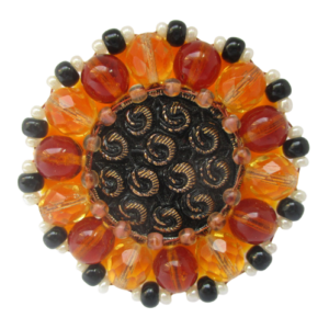 Černozlatá korálková brož. Brož vyrobená z černého jabloneckého knoflíku se zlatým reliéfem, který je opletený pomocí měděného drátku a korálků v hnědé, žluté, černé a perleťové barvě. Je podšitá žlutou plstí. Ze spodní strany je přišitý špendlík ve zlaté barvě.