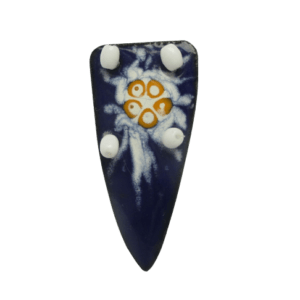 Smaltovaná brož tvaru písmene V s jemnou bílooranžovou kresbou na tmavě modrém podkladu na ručně opracovaném nerezovém plíšku. Podlepená černou plstí s komponentem stříbrné barvy