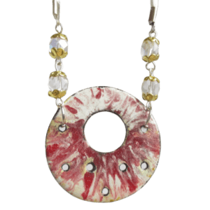 Náhrdelník složený kulatého červenobílého smaltu na ručně opracovaném nerezovém plíšku s nepravidelně umístěnými kruhovými otvory a křišťálových broušených skleněných korálků a komponentů zlaté barvy. Je zavěšený na bílé saténové šňůrce.