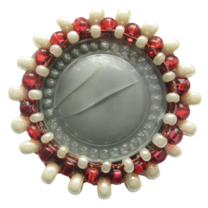 Šedobéžová korálková brož. Brož vyrobená ze šedého jabloneckého knoflíku, který je opletený pomocí měděného drátku a korálků v červené a perleťové barvě. Je podšitá šedou plstí. Ze spodní strany je pomocí průhledného plastu připevněný špendlík ve stříbrné barvě.