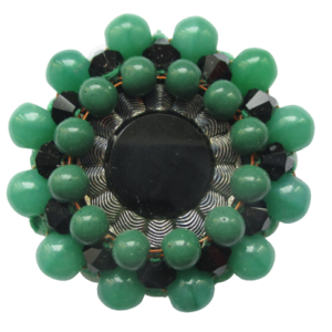 Zelenočerná korálková brož. Brož vyrobená z černého jabloneckého knoflíku se stříbrným okrajem, který je opletený pomocí měděného drátku a korálků v černé a zelené barvě. Je podšitá zelenou plstí. Ze spodní strany je přišitý špendlík ve stříbrné barvě.