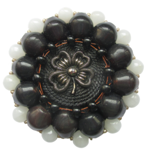 Velká korálková brož. Brož vyrobená z černého jabloneckého knoflíku se stříbrným reliéfem květiny, který je opletený pomocí měděného drátku a korálků v černé a tmavohnědé a bílé barvě. Je podšitá černou plstí. Ze spodní strany je přišitý špendlík ve stříbrné barvě.