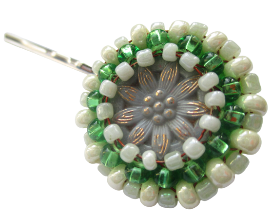 Zelenkavá korálková sponka. Sponka vyrobená z šedého jabloneckého vintage knoflíku s květinovým reliéfem, který je opletený pomocí měděného drátku a korálků ve světle modré, zelené a perleťové barvě. Je podšitá zelenou plstí. Ze spodní strany je pomocí průhledného plastu připevněné pevné bižuterní perko ve stříbrné barvě.