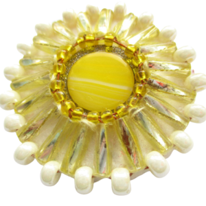 Korálková sluneční brož. Brož vyrobená ze žlutého jabloneckého knoflíku, který je opletený pomocí měděného drátku a korálků ve žluté a perleťové barvě. Je podšitá bílou plstí. Ze spodní strany je přišitý špendlík ve zlaté barvě.