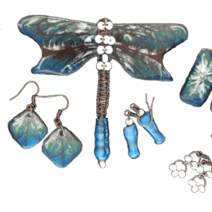 Smaltovaná souprava s tyrkysovou vážkou. Dominantním prvkem je smaltovaná brož vážka s tyrkysovými křídly a drátkovaným tělem zdobeným korálky. Tento sofistikovaný a výrazný šperk je symbolem elegance a volnosti. Ke broži si lze vybrat z několika typů náušnic podle příležitosti a osobního stylu.