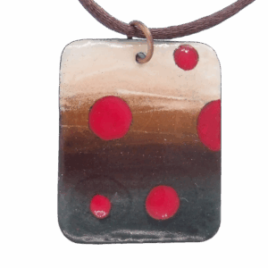 Ručně vyráběný obdélníkový smaltovaný přívěsek s červenými puntíky na přírodním podkladu, zavěšený na měděném kroužku.