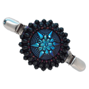 Velká černá korálková oděvní spona s blyštivě fialovým knoflíkem s květinovým reliéfem.